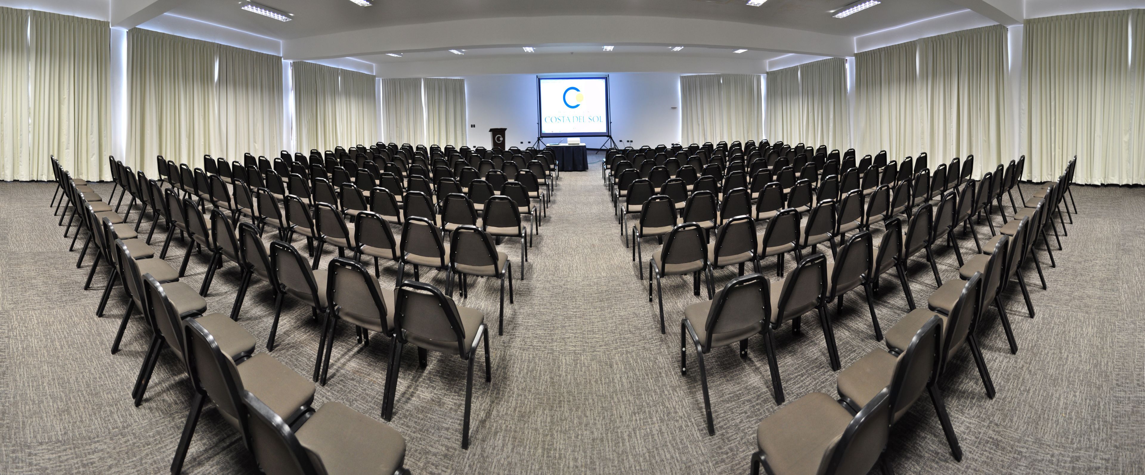 A conference room with rows of chairs facing a projection screen displaying 'COSTA DEL SOL'.