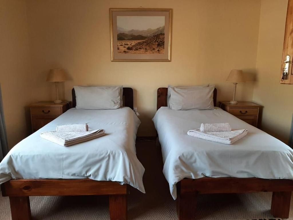 Una habitación con dos camas individuales, cada una con una almohada y una toalla doblada. Hay un cuadro enmarcado en la pared sobre las camas.