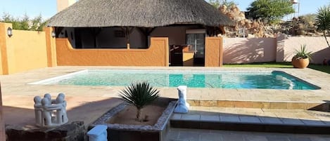 Un área de piscina con una estructura de techo de paja, escalones de piedra y un pequeño jardín con una planta de palma.