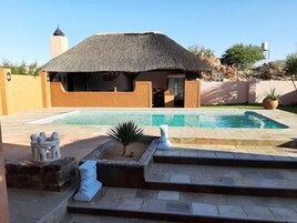 Un área de piscina con una estructura de techo de paja, escalones de piedra y un pequeño jardín con una planta de palma.