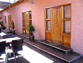 Edificio con puertas y ventanas de madera, una escalera y zona de estar exterior con sillas.