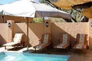 Zona junto a la piscina con sillones y sombrillas.