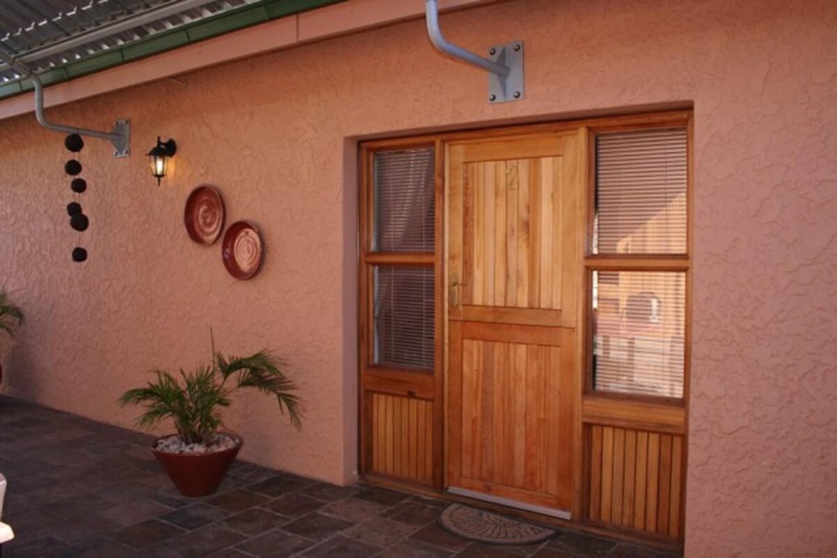 A wooden door with a window, a wall-mounted light fixture, and a potted plant.