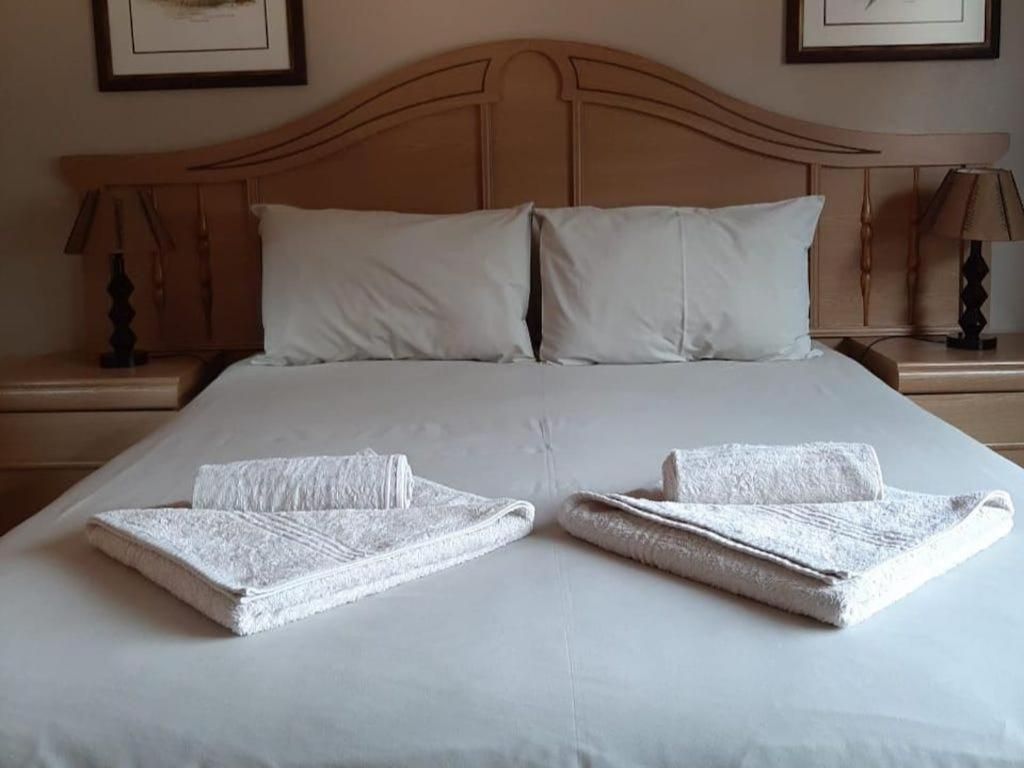 A neatly made bed with two pillows and two folded towels on a white bedspread.