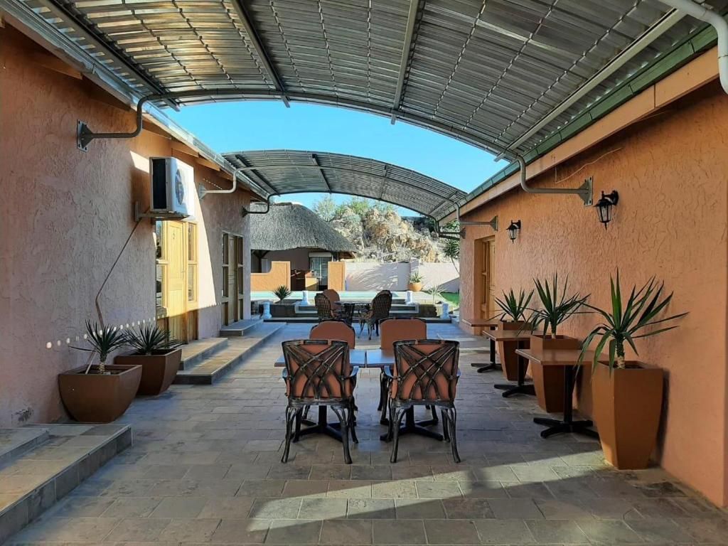 An outdoor patio area with a covered seating area, potted plants, and a thatched-roof structure in the background.