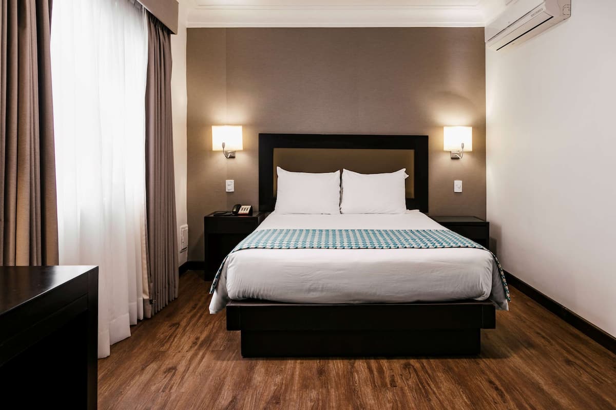 Ein Hotelzimmer mit einem großen Bett, zwei Nachttischen, einem Beistelltisch und einem Schreibtisch.