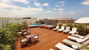 A rooftop deck with a swimming pool, lounge chairs, and a dining area.