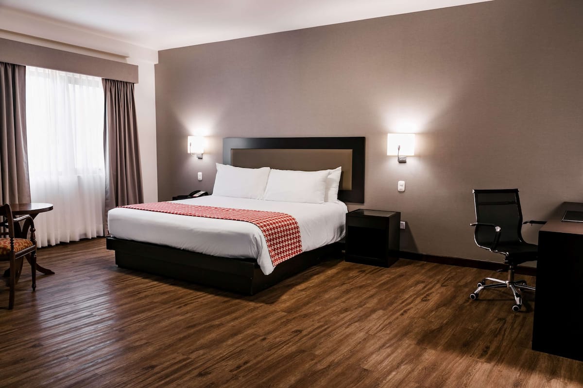 Ein Hotelzimmer mit einem großen Bett, Nachttischen, einem Schreibtisch und einem Sessel.