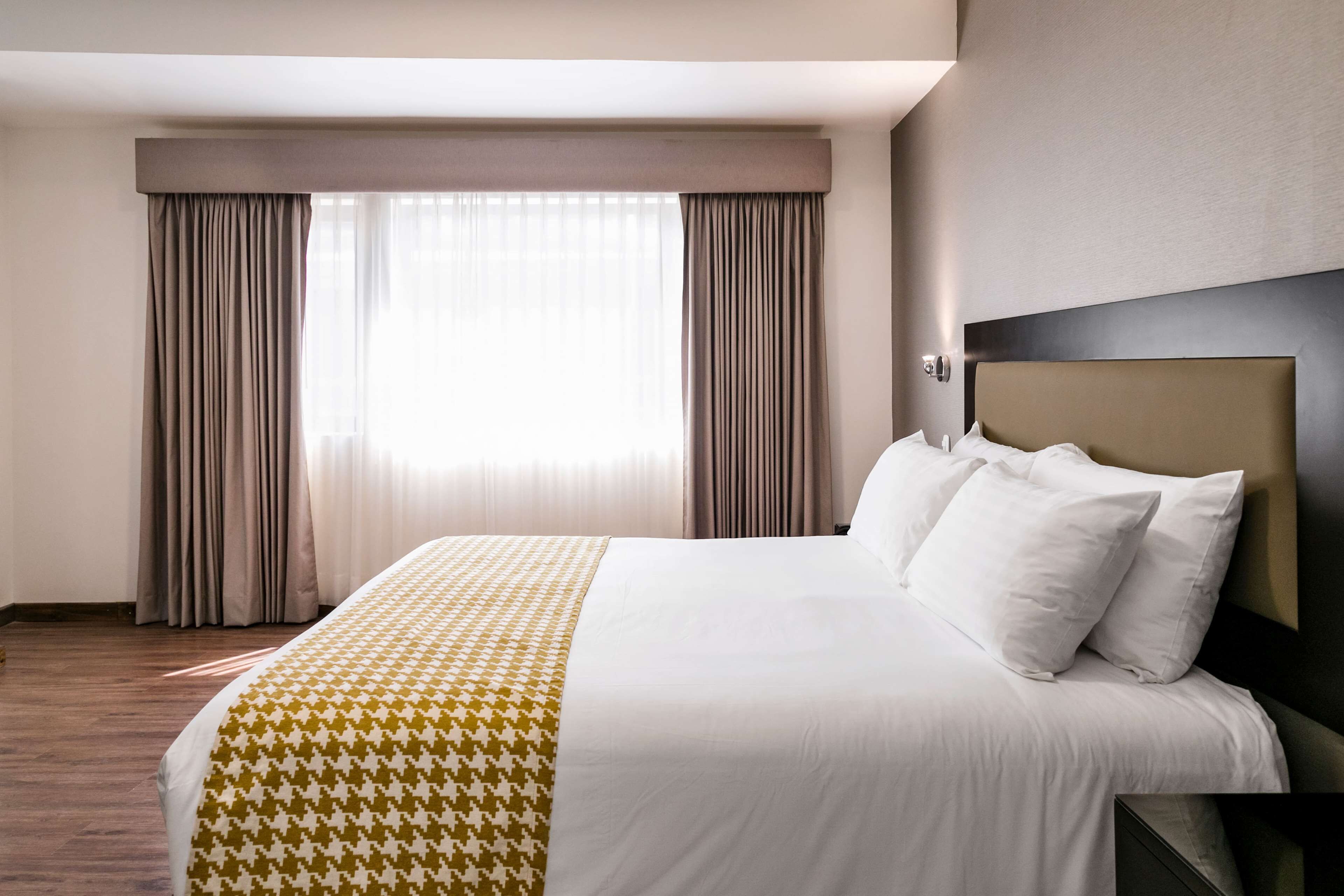 A hotel room with a large bed, a headboard, and a window with curtains.