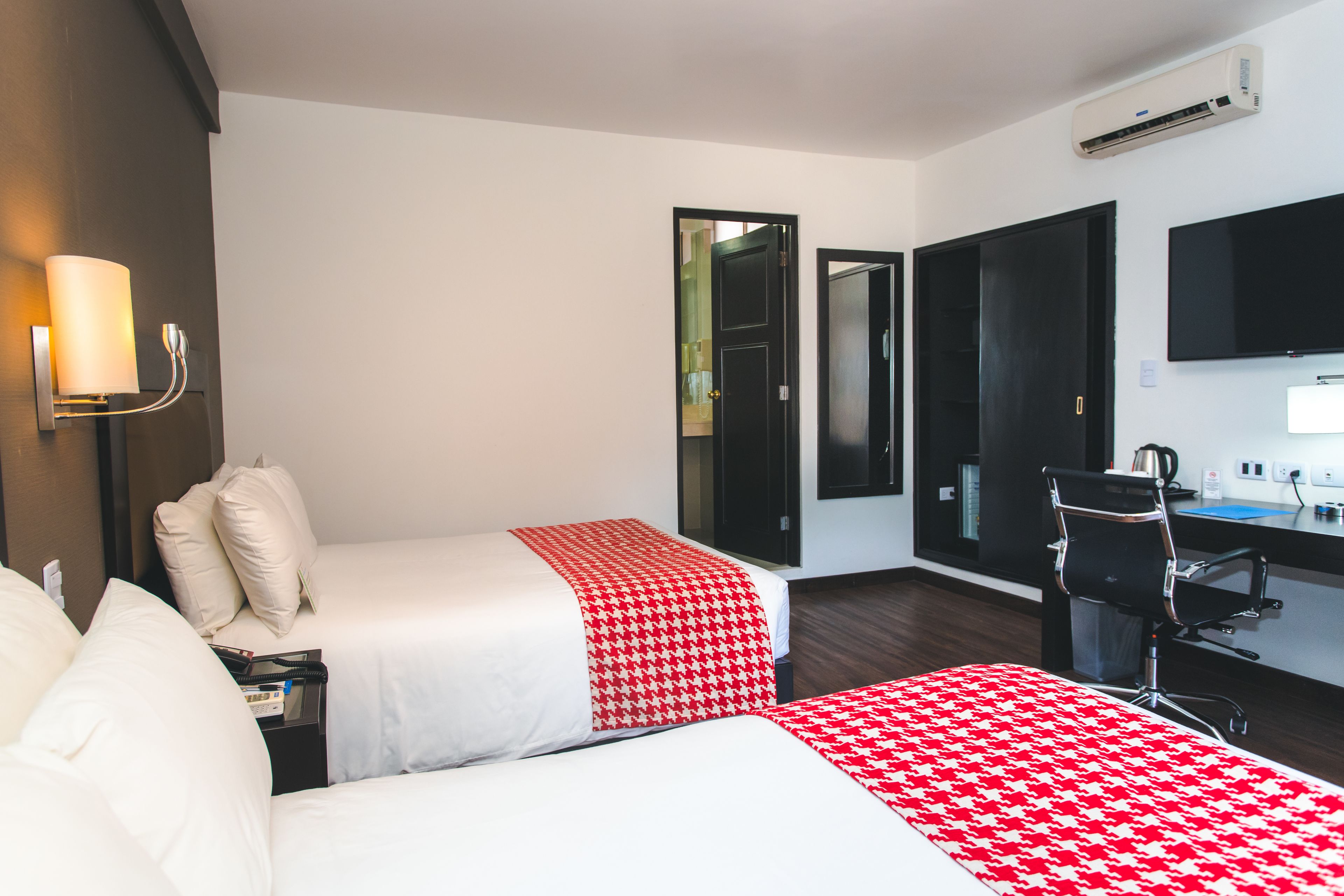 Habitación de hotel con dos camas, un escritorio, una silla, un televisor y un aire acondicionado.
