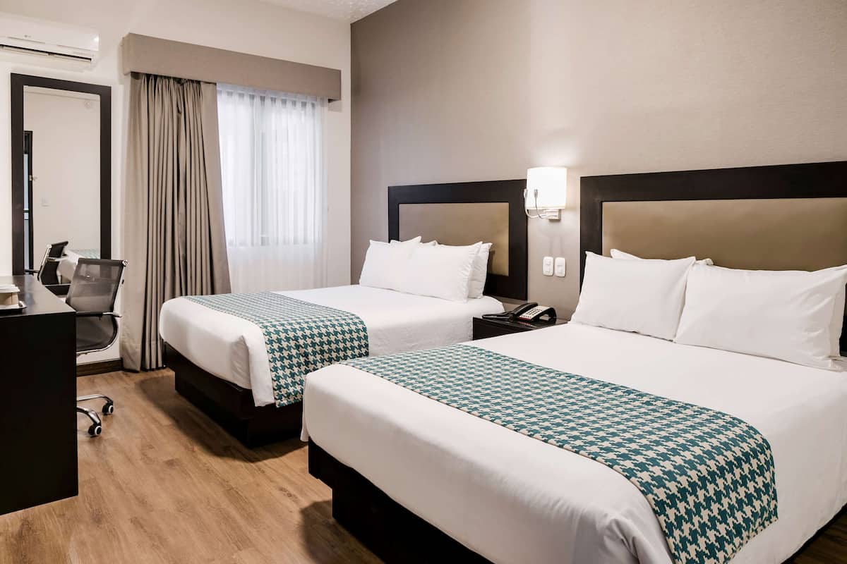 Ein Hotelzimmer mit zwei Betten, einem Schreibtisch, einem Stuhl, einem Telefon und einem Fenster mit Vorhängen.