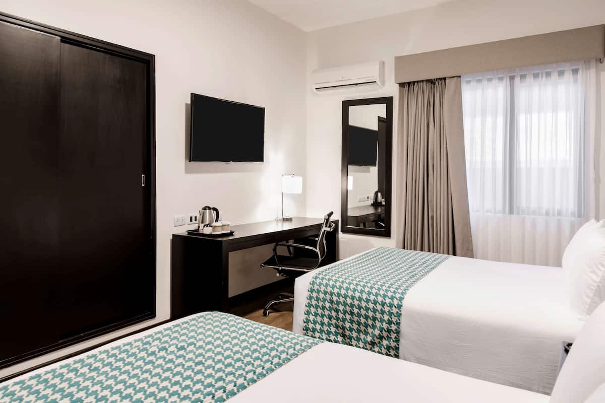 Ein Hotelzimmer mit zwei Betten, einem Schreibtisch, einem Stuhl, einem Fernseher und einem Kleiderschrank.