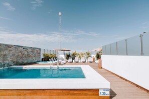 Area piscina sul tetto con cielo azzurro, muro in pietra e terrazza in legno.