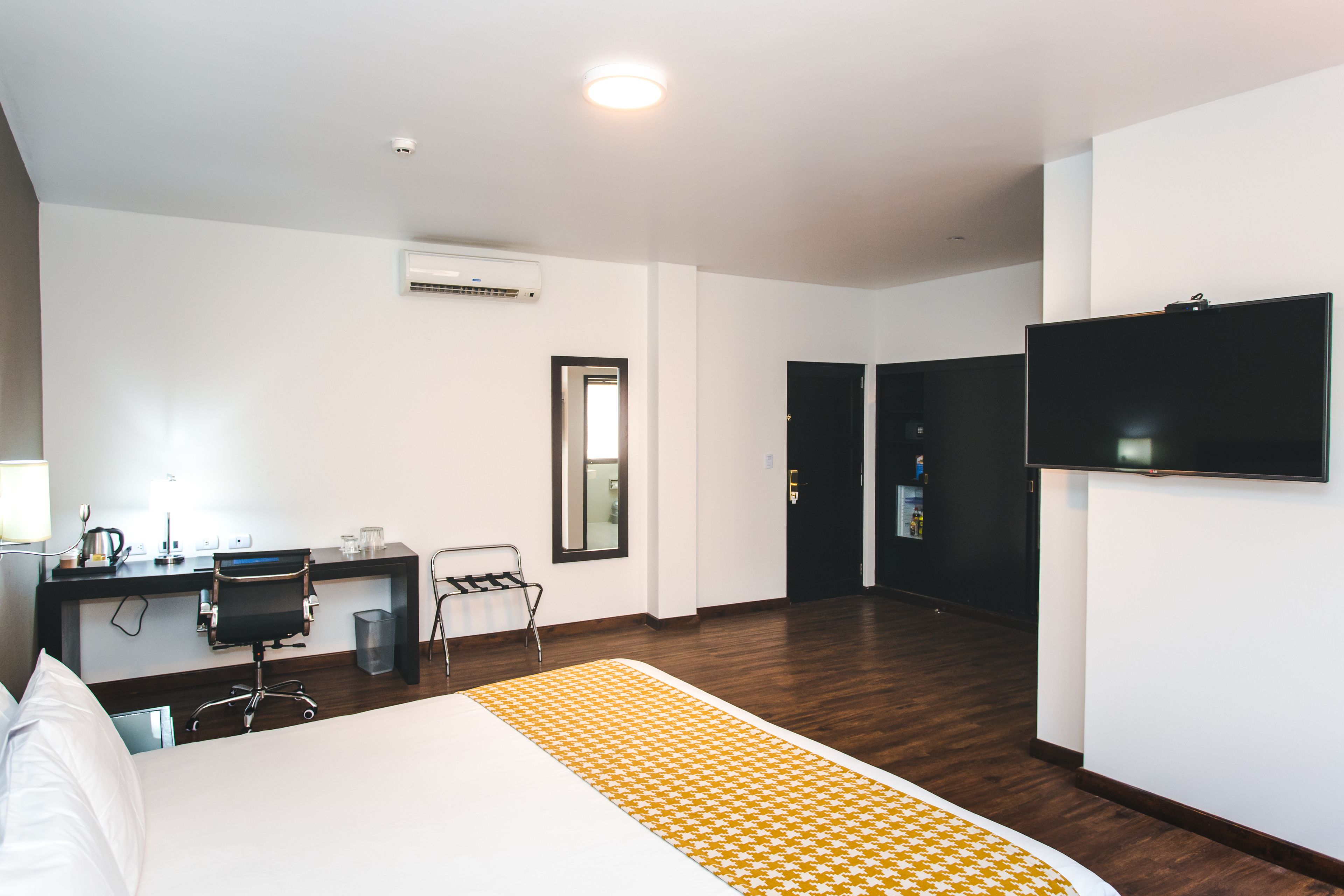 Una habitación de hotel con cama, escritorio, silla, televisor y espejo.