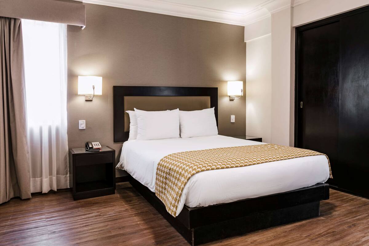 Ein Hotelzimmer mit einem großen Bett, Nachttischlampen, einem Telefon und einem dunklen Holzschrank.