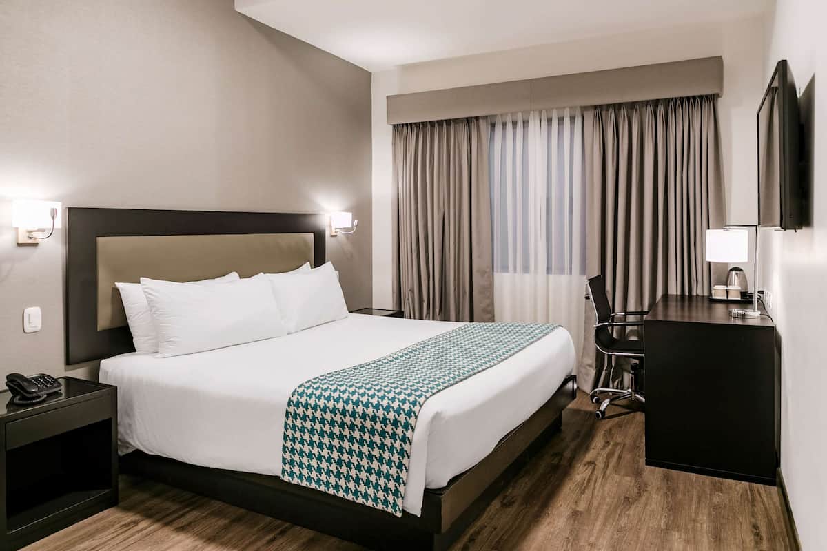 Ein Hotelzimmer mit einem großen Bett, Nachttischlampen, einem Schreibtisch mit Stuhl und einem Fernseher.