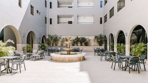 A spacious outdoor patio with multiple tables and chairs, a central fountain, and surrounding greenery.