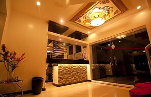 Un hall d’hôtel moderne avec un comptoir d’accueil, une horloge et un plafond décoratif.
