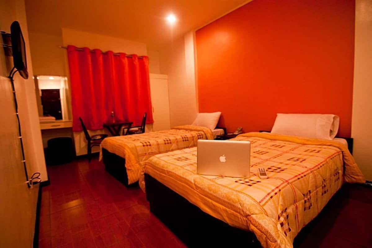 A hotel room with two beds, a desk, and a laptop on one bed.
