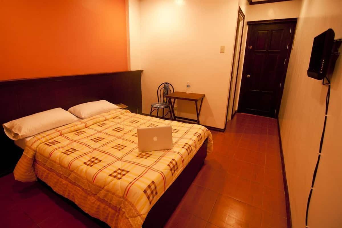 A hotel room with a bed, a laptop on the bed, a chair, a small table, and a door.