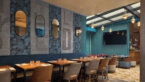 A restaurant interior with a modern design, featuring a blue and grey color scheme, wooden tables and chairs, and a large TV screen on the wall. - Le Robinet d'Or (Paris)