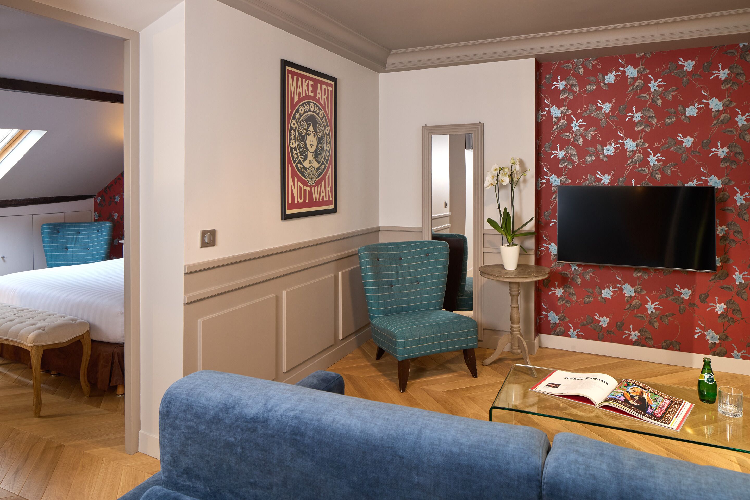 Ein modernes Wohnzimmer mit einer Couch, einem petrolfarbenen Sessel, einem Glastisch, einem Flachbildfernseher und floralem Wandpapier.