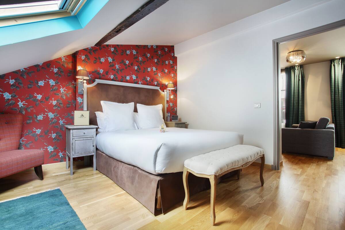 Un dormitorio con una cama grande, una mesita de noche, un banco, un sofá rojo y un espejo.