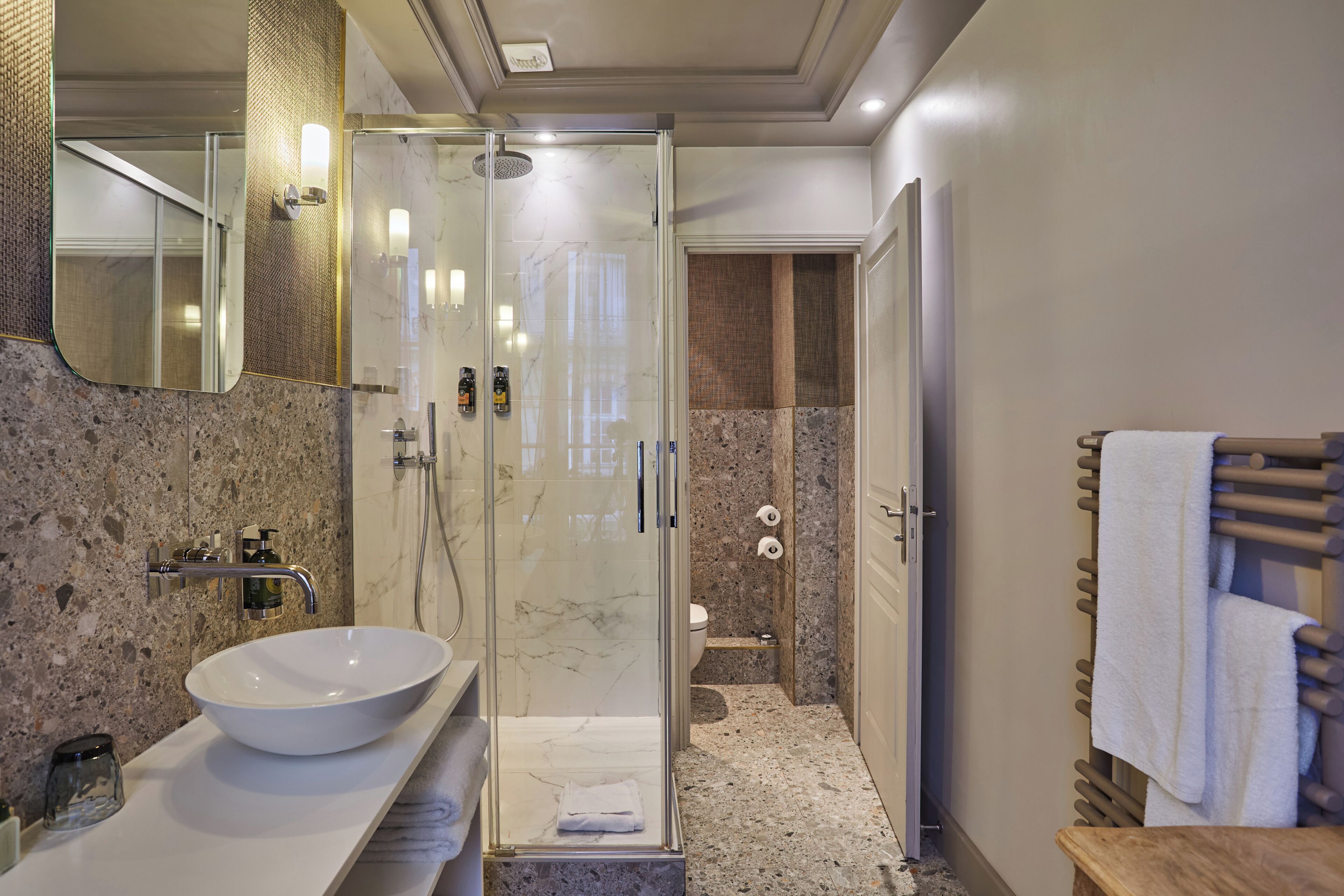 A modern bathroom with a glass-enclosed shower, a marble sink, and a wooden towel rack.