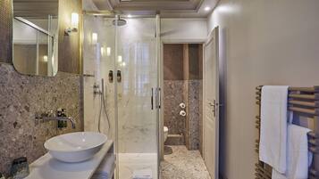 A modern bathroom with a glass-enclosed shower, a marble sink, and a wooden towel rack.