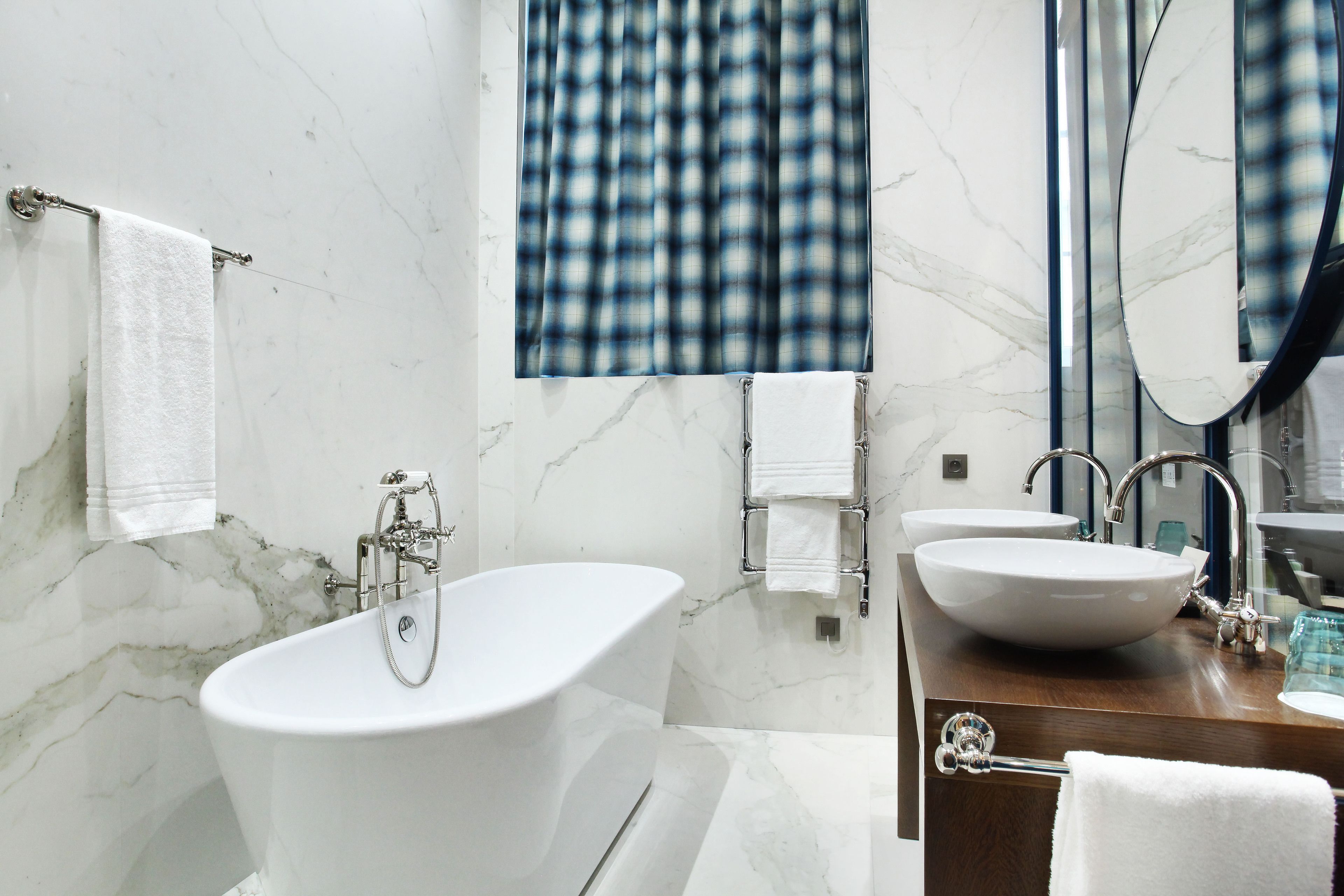 A modern bathroom with a freestanding bathtub, two sinks, a large mirror, and a blue plaid shower curtain.