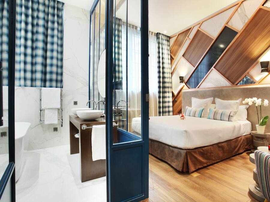 A modern hotel room with a large bed, a bathroom with a sink and mirror, and a view of the outside.