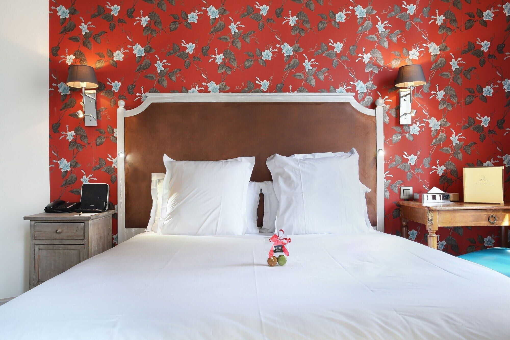 A neatly made bed with white linens, a wooden headboard, and a floral wallpaper pattern.