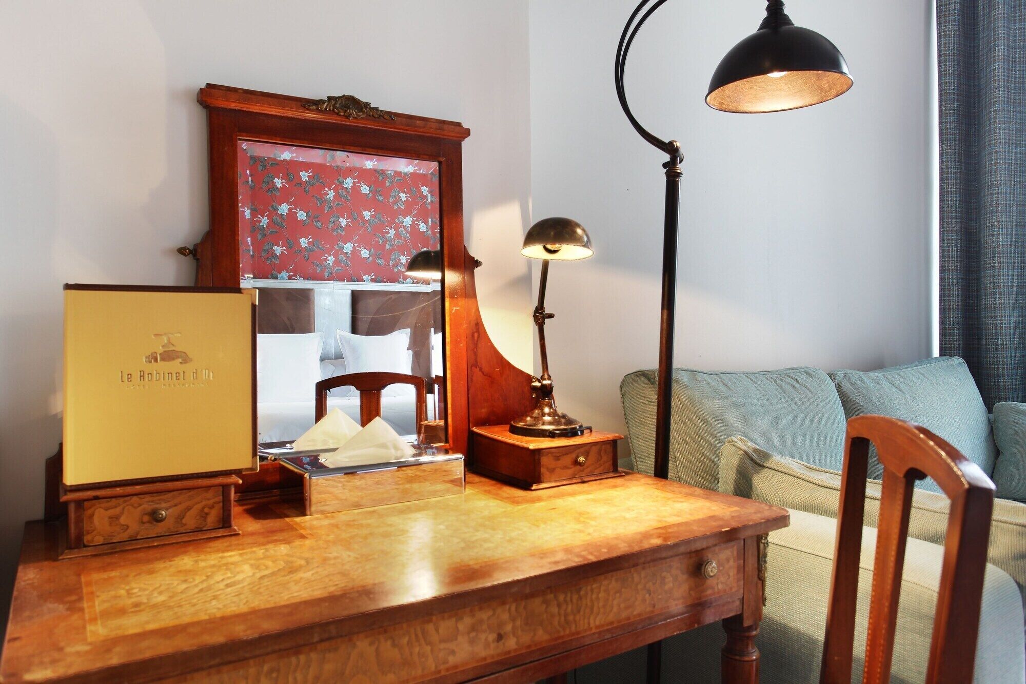 Un bureau en bois orné d’un miroir encadré, d’une lampe et d’un livre intitulé « Le Robinet d’Heure ».