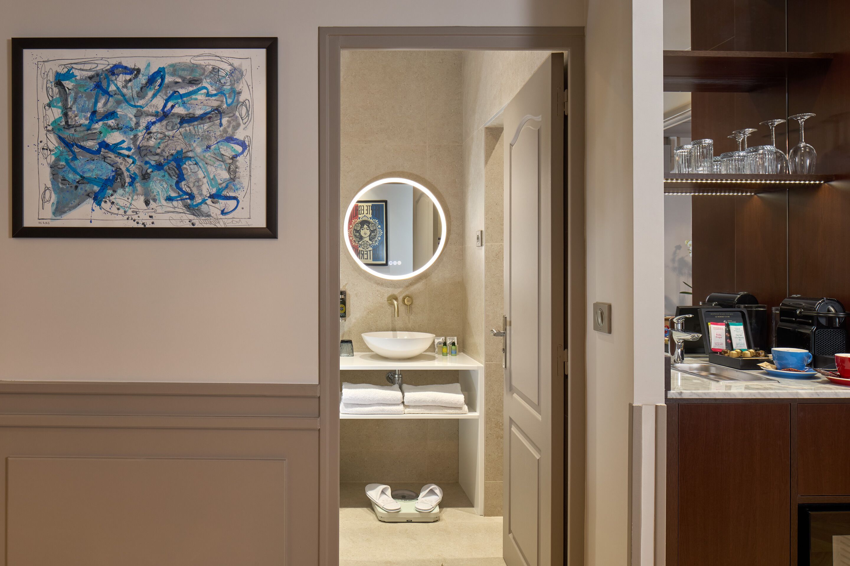 A hotel bathroom with a sink, mirror, and toilet. There is a framed abstract painting on the wall.
