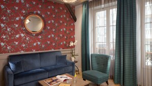 A room with a blue sofa, a round mirror, a potted orchid, and a window with curtains. - Le Robinet d'Or (Paris)