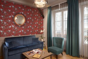 A room with a blue sofa, a round mirror, a potted orchid, and a window with curtains. - Le Robinet d'Or (Paris)
