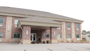 A brick building with a covered entrance, a parking lot, and a sign indicating 'OPEN'. - Bell's Extended Stay and Suites (St. Robert)