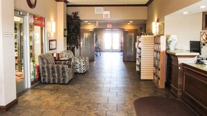 A hotel lobby with a reception desk, a convenience store, seating area, and a large plant. - Bell's Extended Stay and Suites (St. Robert)