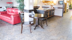 A lobby with a red leather sofa, a round table, and chairs, a potted plant, and a kitchenette area. - Bell's Extended Stay and Suites (St. Robert)