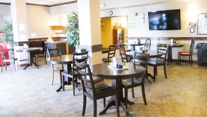 A restaurant with multiple tables and chairs, a television mounted on the wall, and a clock on the wall. - Bell's Extended Stay and Suites (St. Robert)