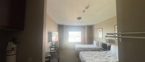 A hotel room with two beds, a desk, a chair, and a window providing natural light.