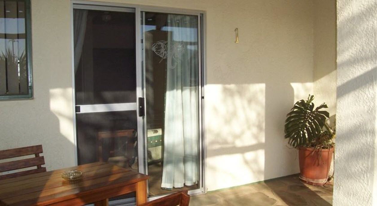 A patio with a wooden table and chairs, a sliding glass door, and a potted plant.