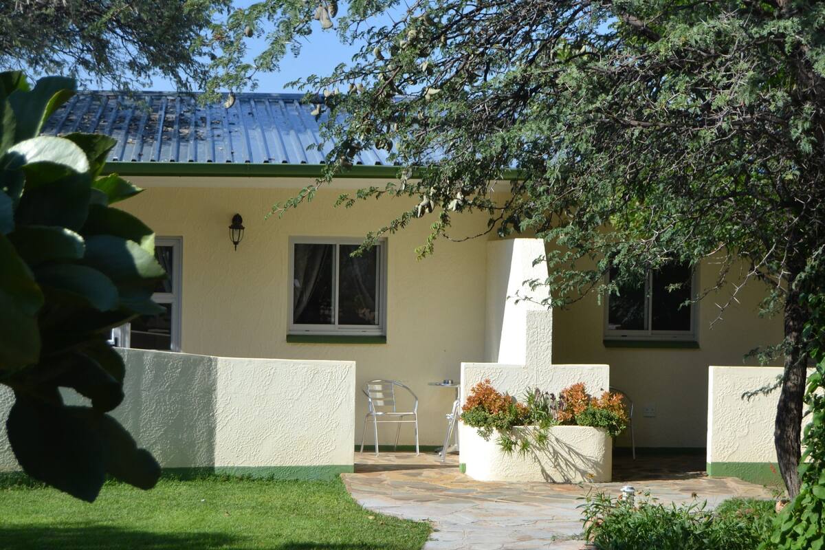 A house with a tiled roof, a small patio with a chair, and a garden area with plants.