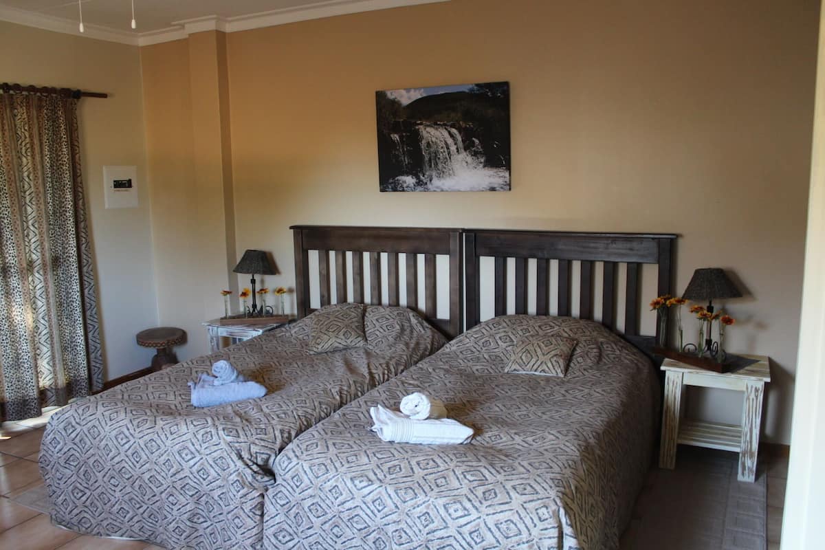 A hotel room with two beds, a painting of a waterfall on the wall, and a curtain with a leopard print.