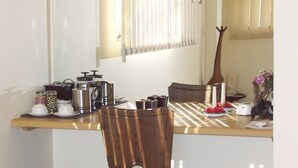 Ein Essbereich mit einem Holztisch, Stühlen, einer Kaffeemaschine, einem Wasserkocher und einer Vase mit Blumen.