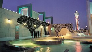A modern hotel pool area with a circular pool, a covered seating area, and a prominent tower in the background. - Hotel Chuo Oasis (Osaka)