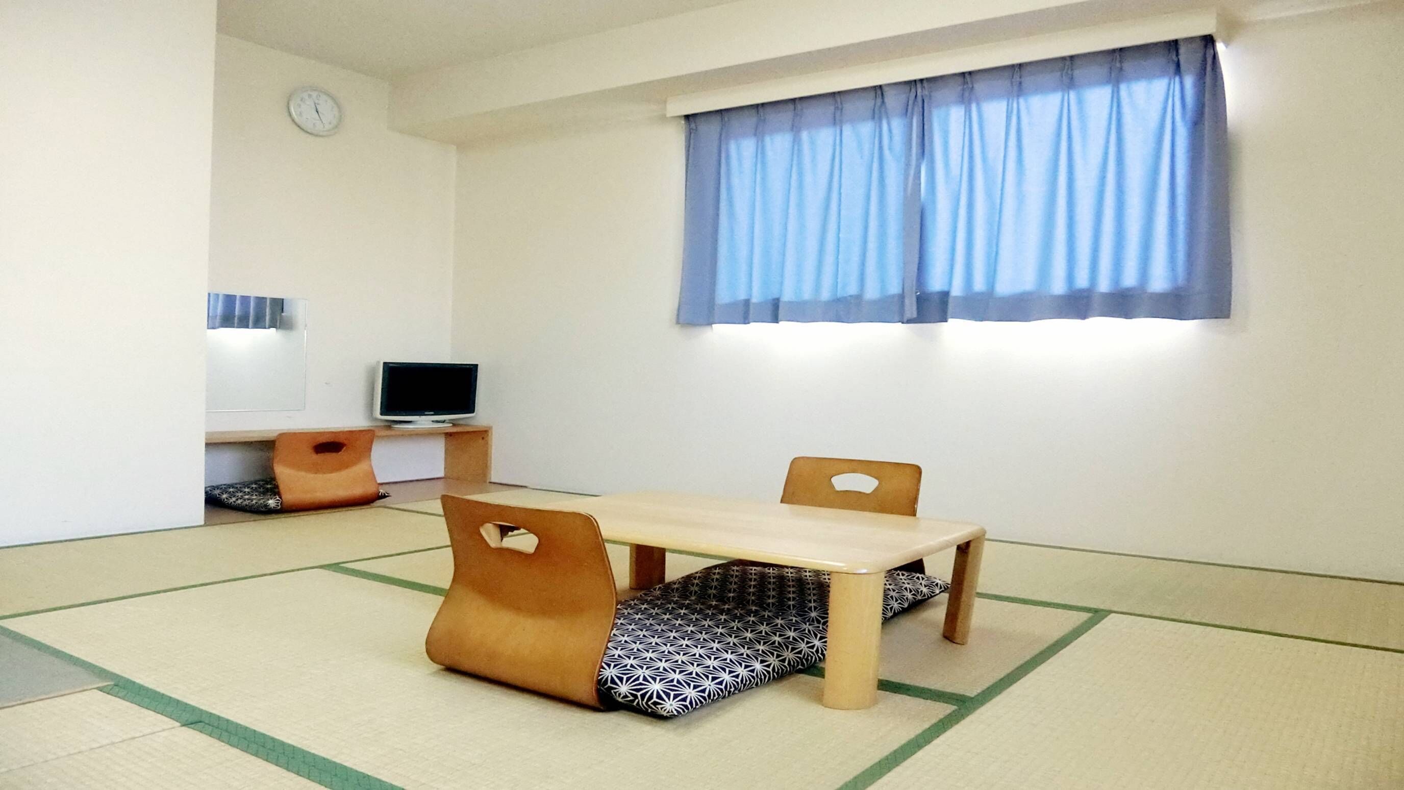 A room with a wooden table, two chairs, a television, and a clock on the wall.