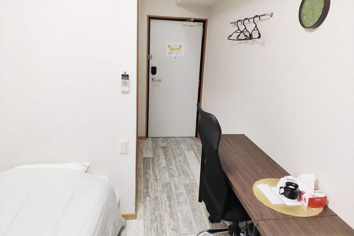 Une chambre d’hôtel comprenant un lit, un bureau avec une chaise, une horloge et un porte-manteau.