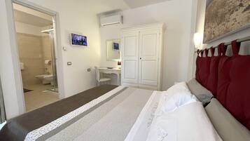 Habitación con cama, escritorio, silla, armario, zona de ducha y televisor.