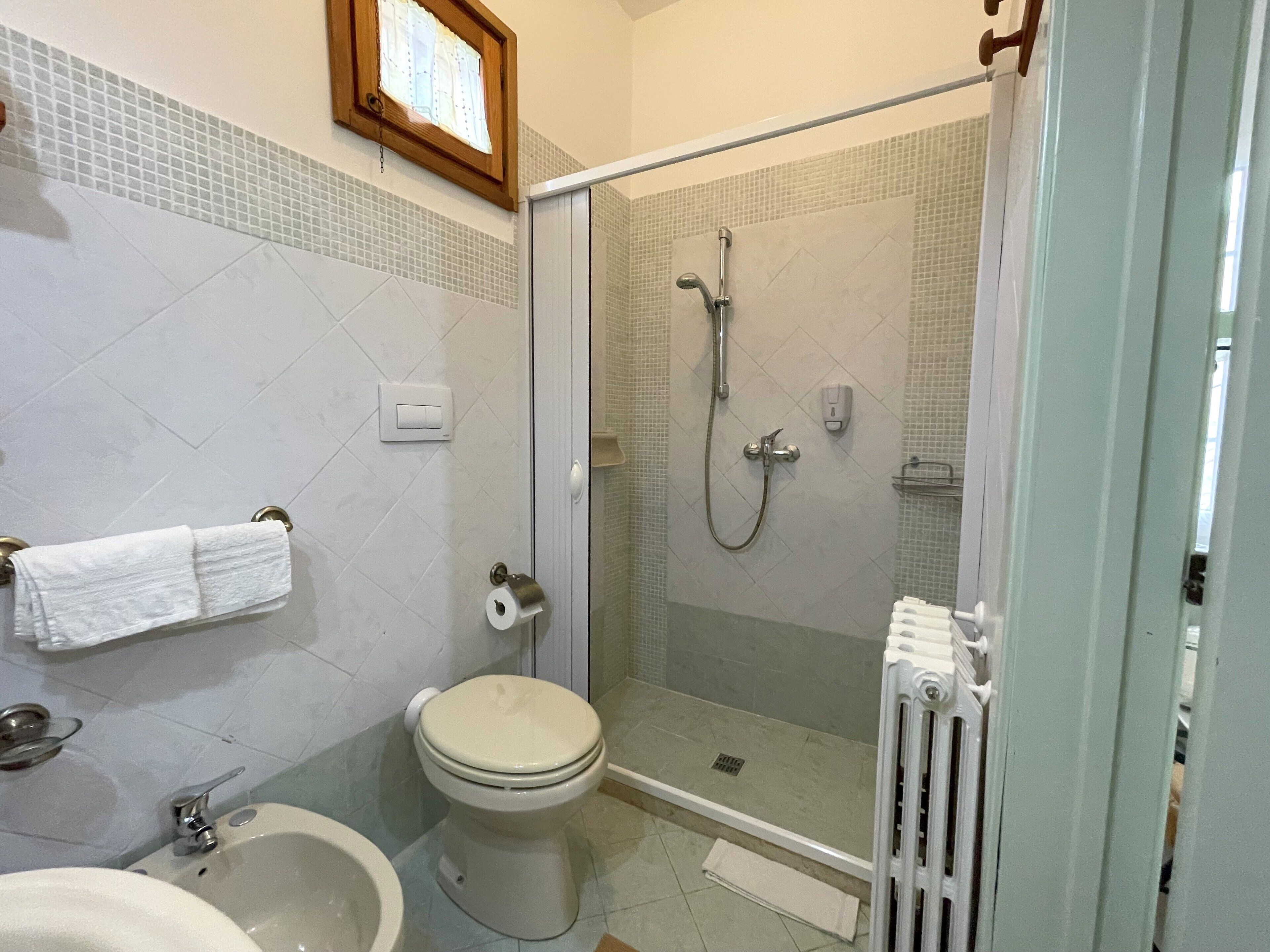Un baño con inodoro, bidé, lavabo y una zona de ducha con mampara de vidrio.